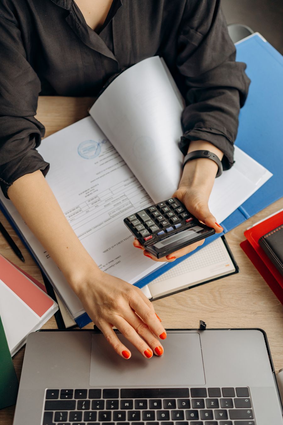 Hands using a calculator while reviewing financial documents beside a laptop